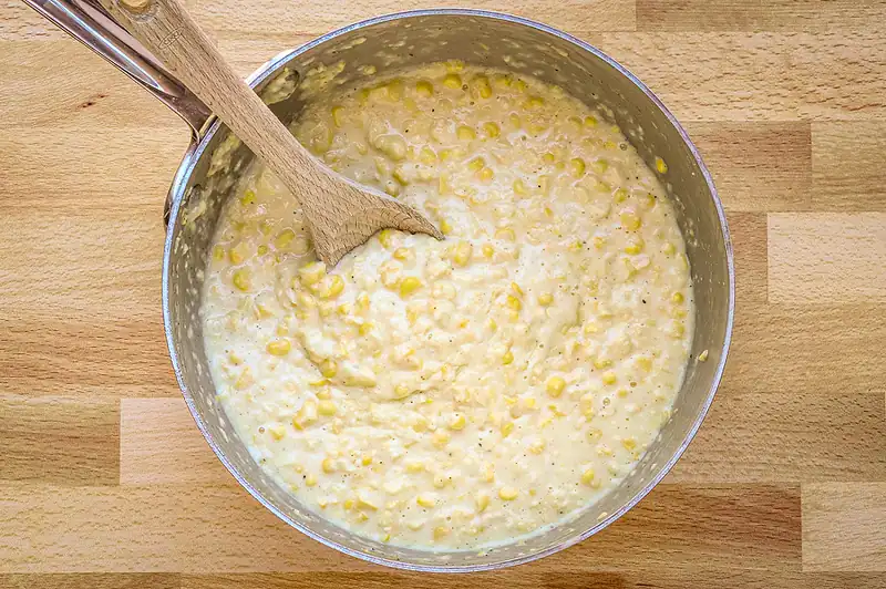 Creamy corn mixture in a metal bowl on a wooden surface.