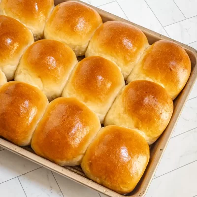 Golden, freshly baked dinner rolls with shiny tops in a baking dish.