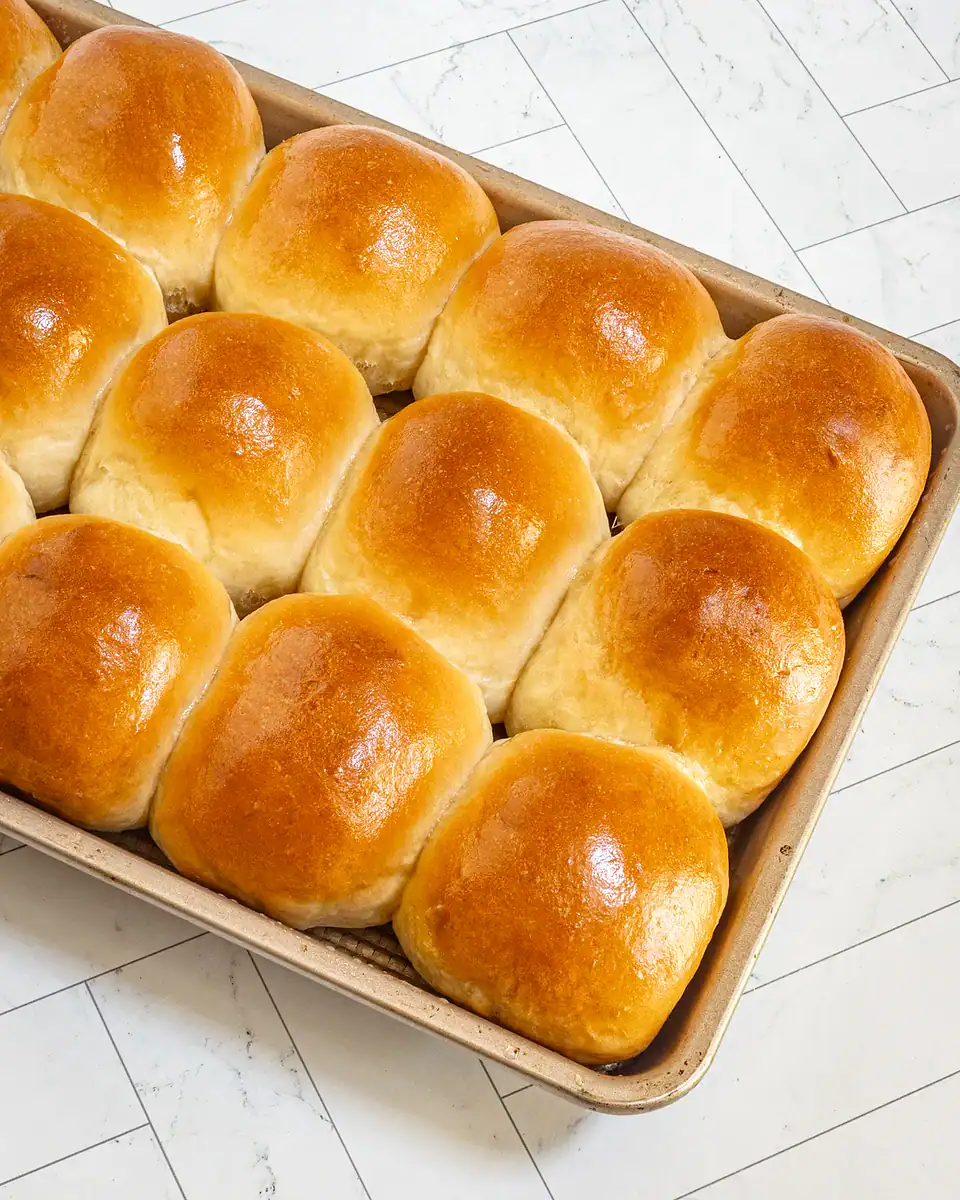 Golden, freshly baked dinner rolls with shiny tops in a baking dish.