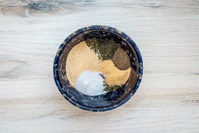 Dried herbs and spices in a black bowl on a wooden surface.