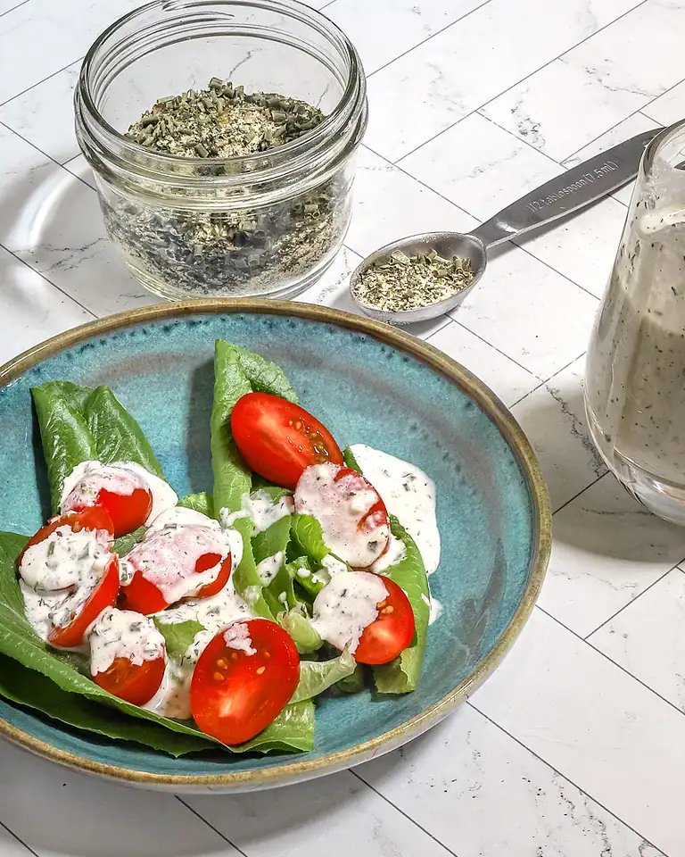 Diced herbs in a glass jar with a spoon and a fresh vegetable salad.