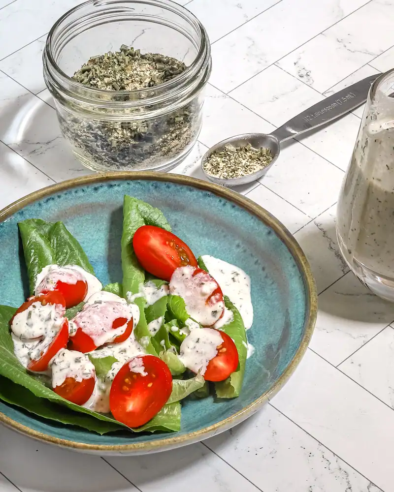 Diced herbs in a glass jar with a spoon and a fresh vegetable salad.