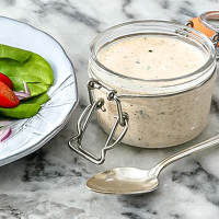 Creamy ranch dressing in glass jar on marble surface.