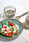 Dried herbs in a glass jar and spoon over a fresh tomato and lettuce salad with creamy dressing on a blue ceramic plate.