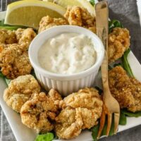 Golden fried chicken bites with lemon wedges and creamy dipping sauce.