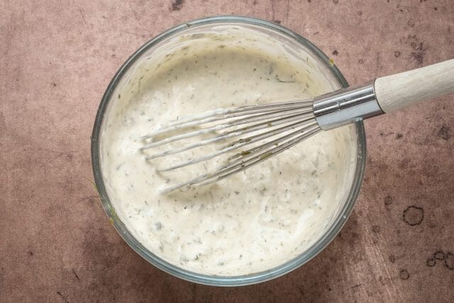 Creamy herb dressing in a glass bowl with a whisk.