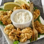 Crispy fried chicken bites with creamy dipping sauce and lemon wedges.