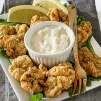 Crispy fried chicken bites with creamy dipping sauce and lemon wedges.