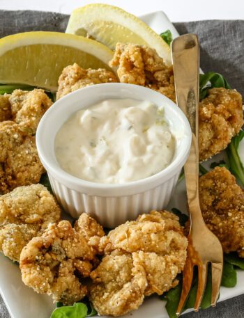 A ramekin with homemade tartar sauce shown with fried oysters.