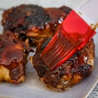 Brushing honey and peanut glaze over baked chicken thighs.