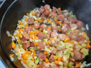 Sautéed vegetables with sliced hot dogs in a pot.