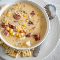 A bowl of hot dog chowder with mini saltines.
