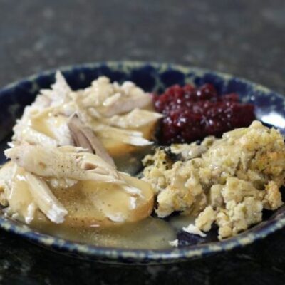 a hot turkey sandwich with leftover stuffing, cranberry sauce, and gravy