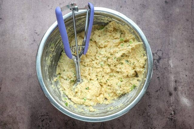 Creamy potato mixture with green onion bits in a metal bowl.
