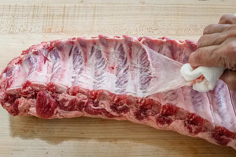 Raw pork ribs with a person extracting the membrane.