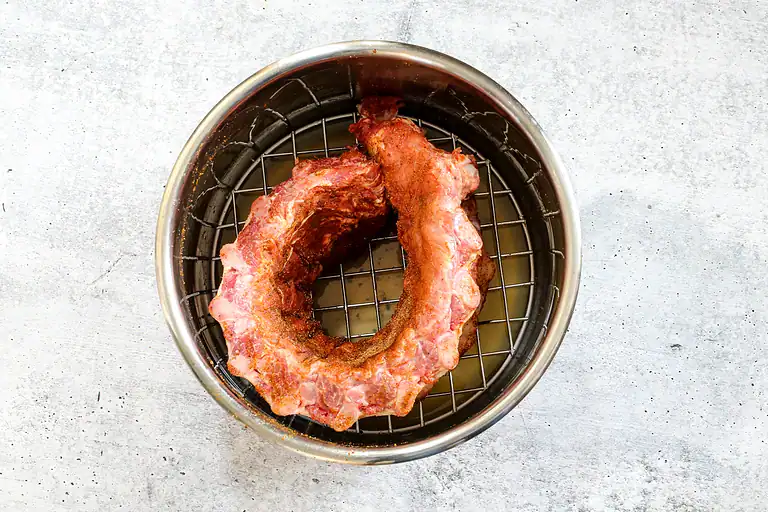 Raw pork neck roast in a metal air fryer basket.