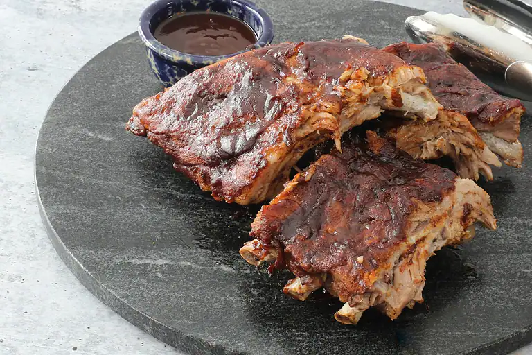 Roasted pork ribs with barbecue sauce on a black stone platter.