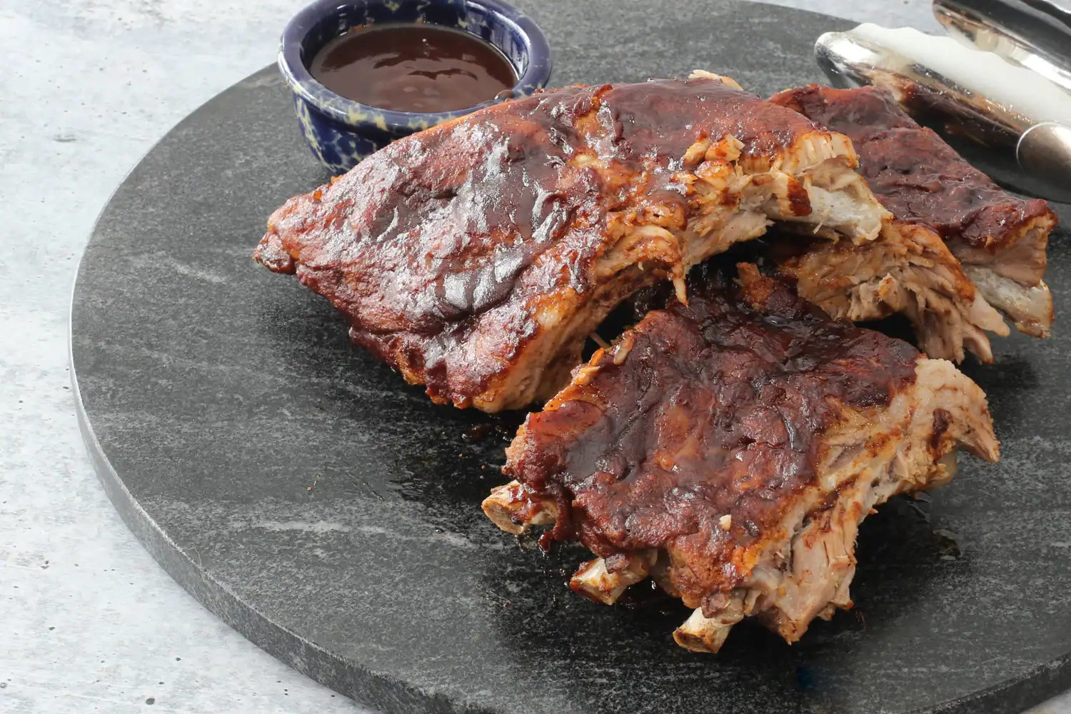 Instant Pot pressure cooker ribs on a slab of black marble with extra sauce.
