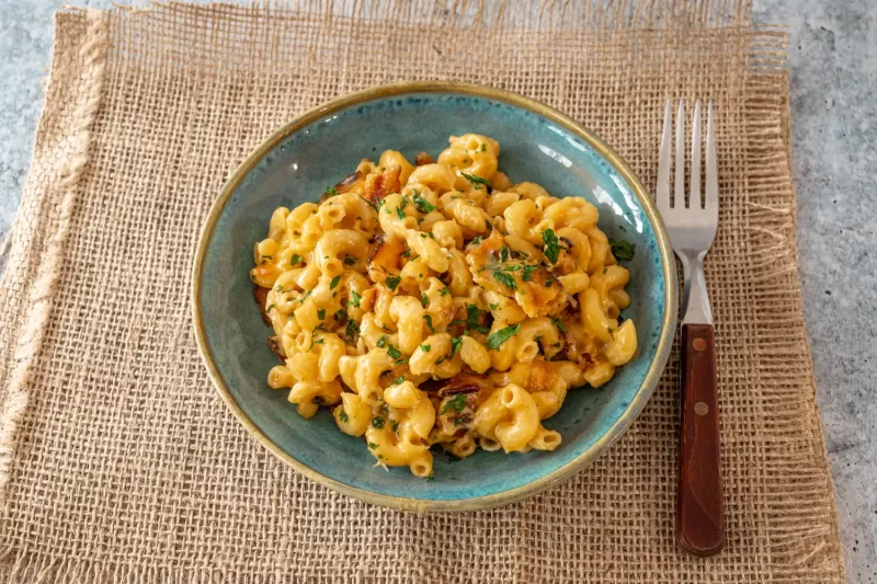Creamy macaroni and cheese topped with herbs in a turquoise bowl.