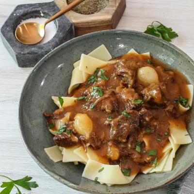 Beef stew with potatoes and noodles in a rustic bowl.