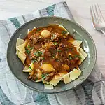 Creamy beef stew over wide egg noodles in a green bowl.