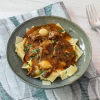 Creamy beef stew over wide egg noodles in a green bowl.