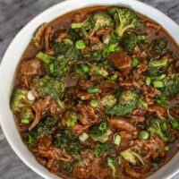 A serving bowl of beef and broccoli with green onion garnish.