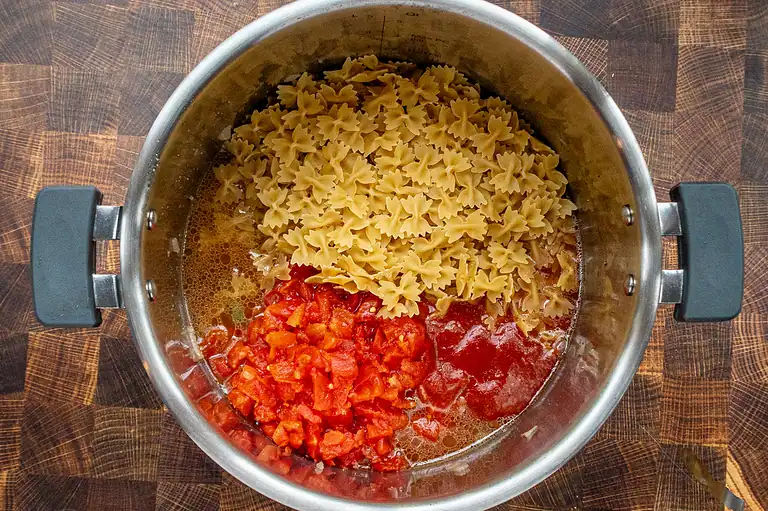 Cooked whole wheat pasta with diced tomatoes and tomato sauce in a stainless steel pot.