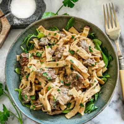 A bowl of Instant Pot beef stroganoff with parsley and arugula.