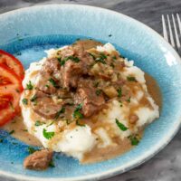 Instant Pot beef tips and gravy on mashed potatoes with tomatoes on the side.