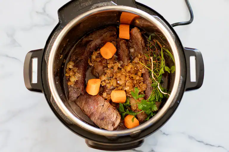 Slow-cooked beef with carrots and herbs in a pressure cooker.