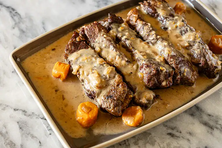 Tender beef ribs in creamy gravy with caramelized carrots on a white dish.