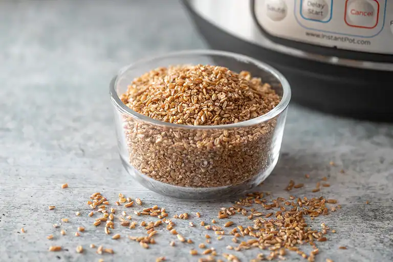 Freshly toasted buckwheat grains in a glass bowl on gray wooden surface.