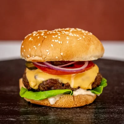 Burger with melted cheese, lettuce, tomato, onions, and beef patty on a toasted sesame bun.