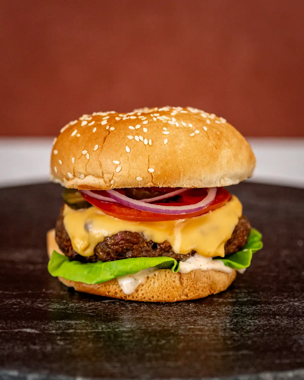 Burger with melted cheese, lettuce, tomato, onions, and beef patty on a toasted sesame bun.