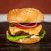 Gourmet cheeseburger with lettuce, tomato, pickles, and onion on a sesame bun.