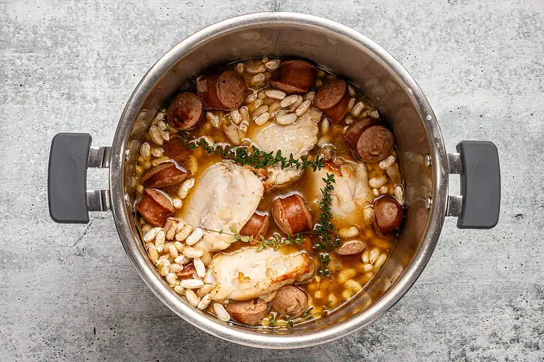 Sausage slices, chicken breasts, and pearl barley cooking in a pot.