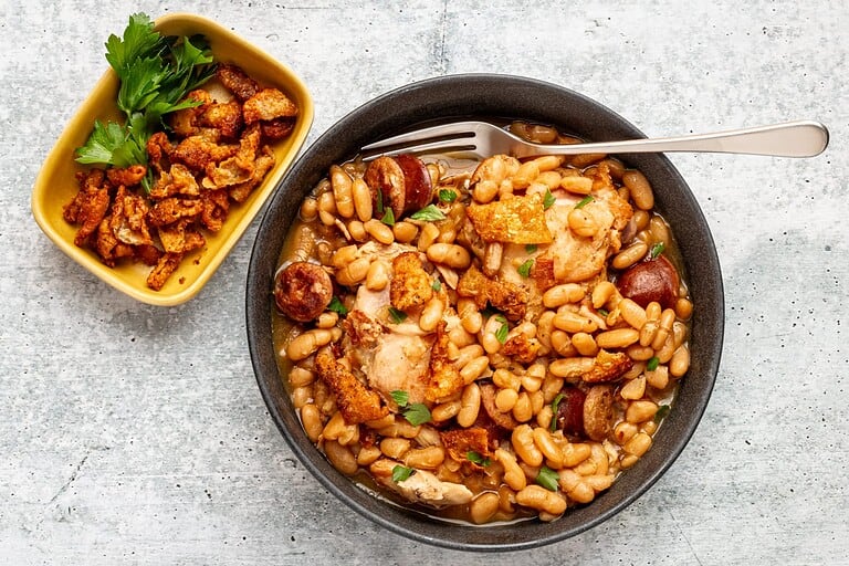 Baked chicken with beans and sausage served in a black bowl.