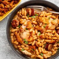 A serving bowl of Instant Pot cassoulet with crispy fried chicken skin and parsley for garnish.