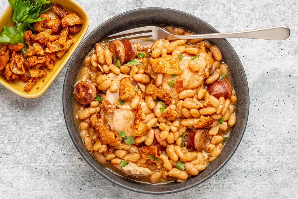 A serving bowl of Instant Pot cassoulet with crispy fried chicken skin and parsley for garnish.