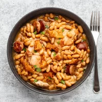 Bowl of white bean and chicken stew with sausage and herbs.