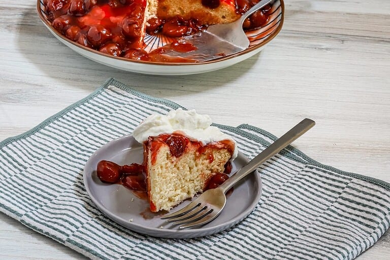 Sweet cherry cobbler with whipped cream on a gray plate.