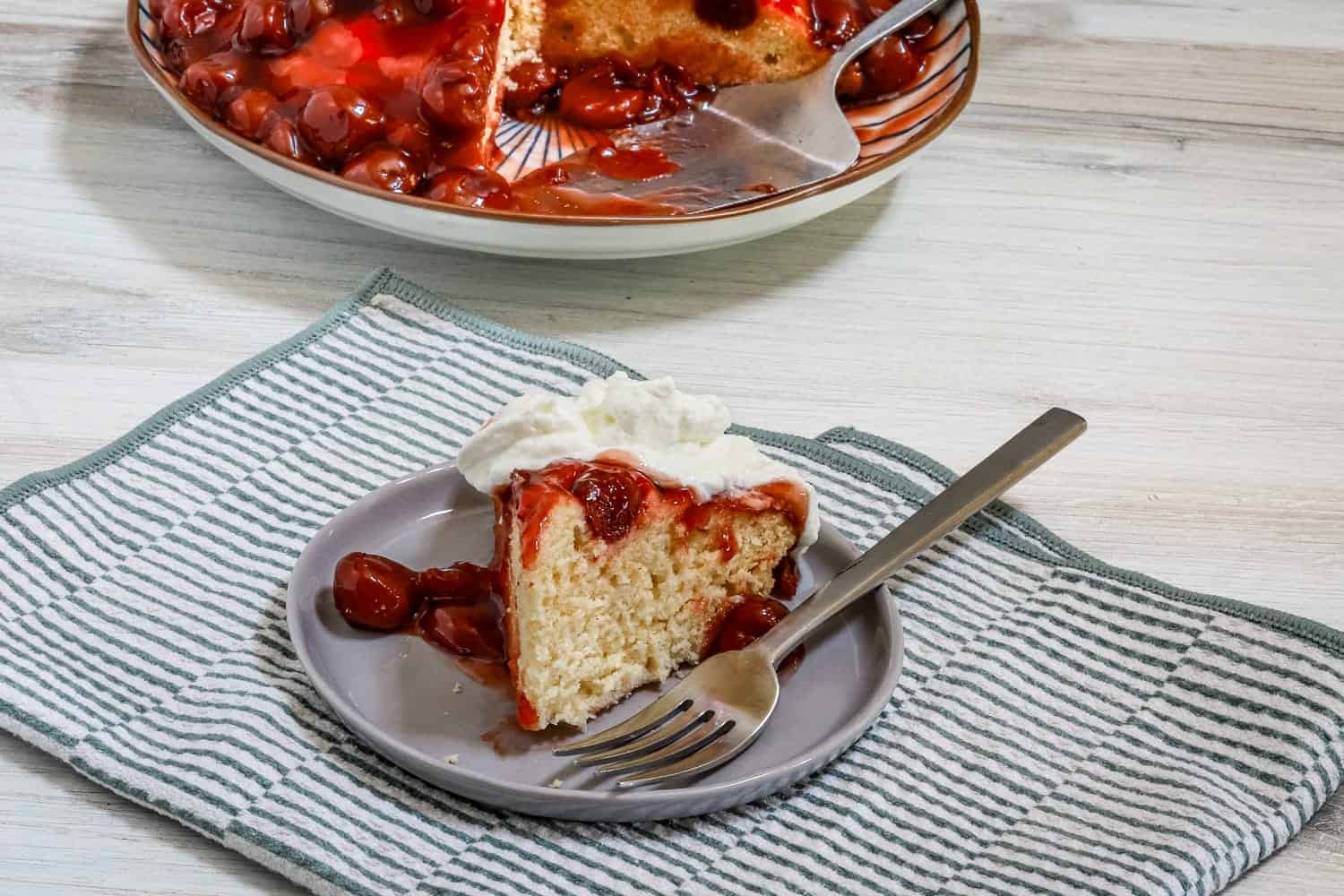 An Instant Pot (instapot) cherry upside-down cake, sliced and served with a whipped cream topping.