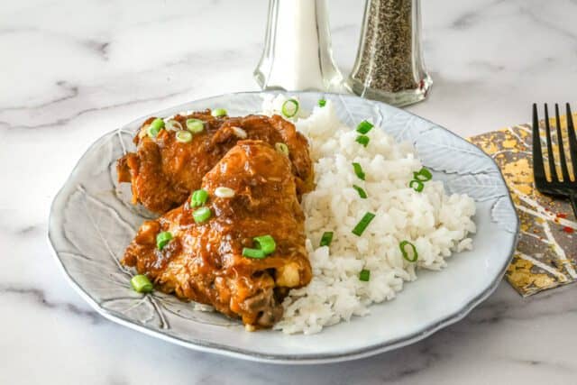 Golden fried chicken thigh with rice and green onions on a white plate.