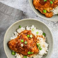 Instant Pot chicken adobo is plated in a bowl with rice and green onions.