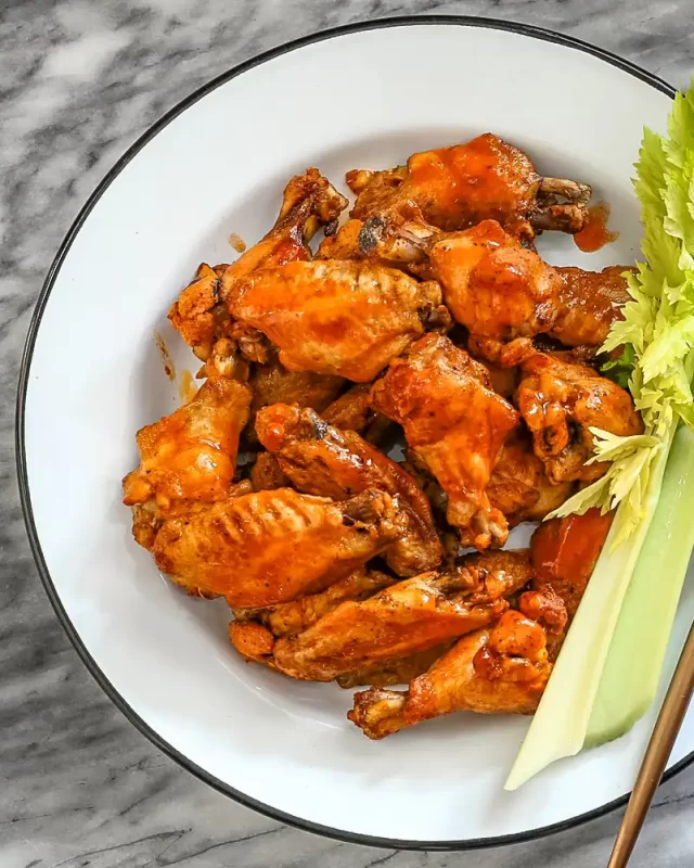 Crispy buffalo chicken wings with celery sticks and greens.