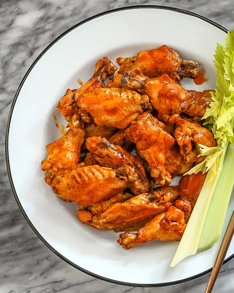 Crispy buffalo chicken wings with celery sticks and greens.