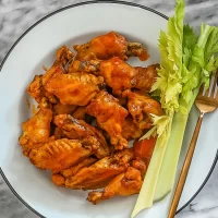 Crispy buffalo chicken wings with celery sticks and a fork.