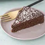 Rich chocolate cake with powdered sugar topping on a white plate.