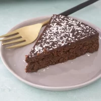 Rich chocolate cake with powdered sugar topping on a white plate.